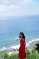 A woman in a red dress standing on a cliff overlooking the ocean.